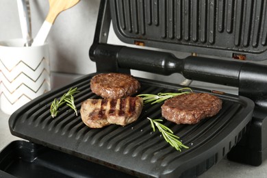 Photo of Open electric grill with beef steak, cutlets and rosemary on grey table, closeup
