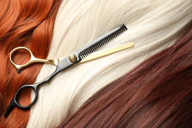 Photo of Strands of different beautiful hair and hairdresser's scissors, top view