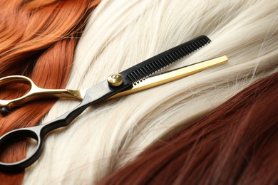 Photo of Strands of different beautiful hair and hairdresser's scissors, closeup