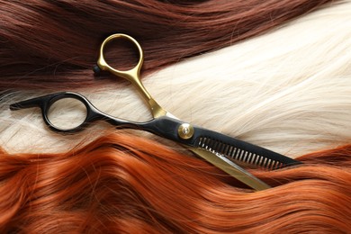 Photo of Strands of different beautiful hair and hairdresser's scissors, above view