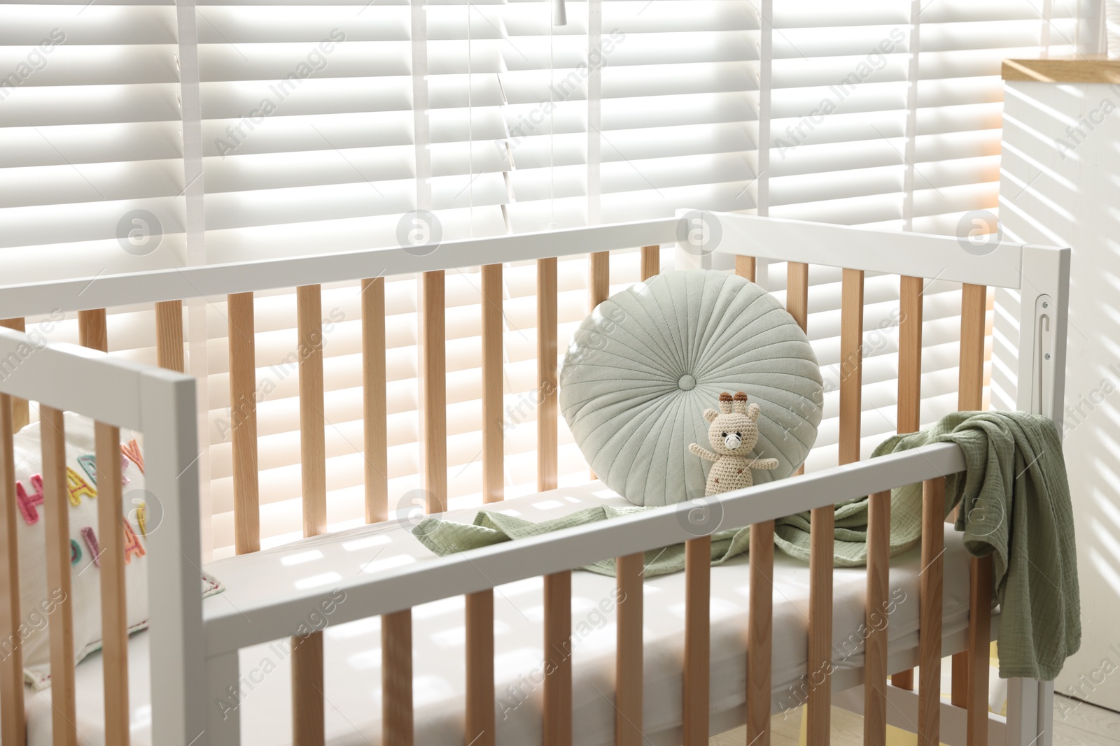 Photo of Crib with cushion, blanket and toy in baby's room