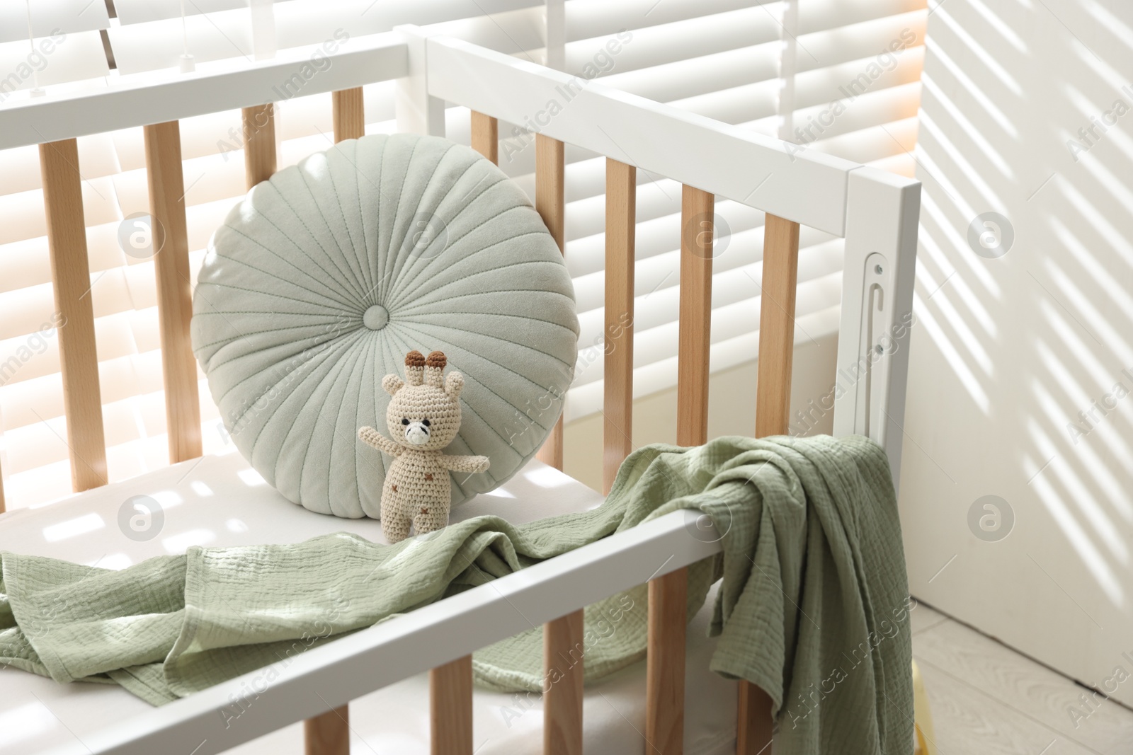 Photo of Crib with cushion, blanket and toy in baby's room, closeup