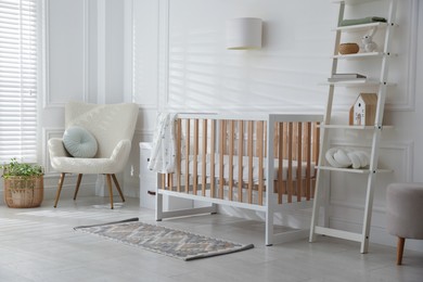 Photo of Stylish baby's room with crib and armchair. Interior design