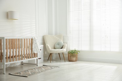 Photo of Stylish baby's room with crib and armchair. Interior design