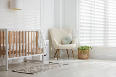 Photo of Stylish baby's room with crib and armchair. Interior design