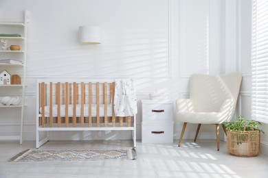 Photo of Stylish baby's room with crib and armchair. Interior design