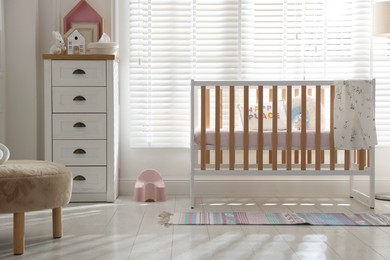 Photo of Stylish baby's room with crib and chest of drawers. Interior design