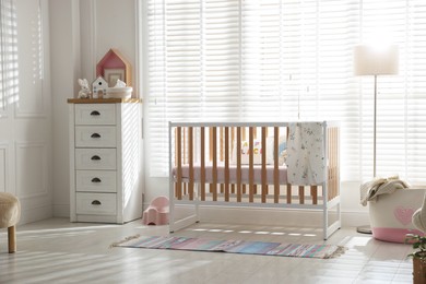 Photo of Stylish baby's room with crib and chest of drawers. Interior design