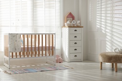Photo of Stylish baby's room with crib and chest of drawers. Interior design