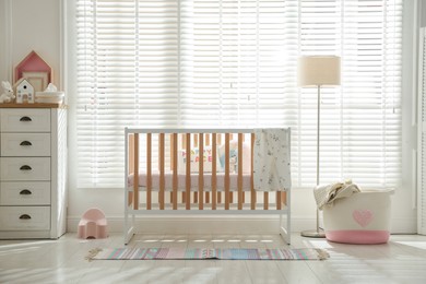 Photo of Stylish baby's room with crib and chest of drawers. Interior design