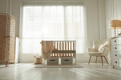 Photo of Stylish baby's room with crib and armchair. Interior design