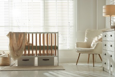 Photo of Stylish baby's room with crib and armchair. Interior design