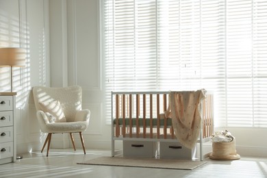 Photo of Stylish baby's room with crib and armchair. Interior design