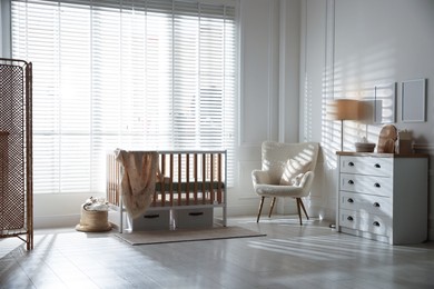 Photo of Stylish baby's room with crib and armchair. Interior design