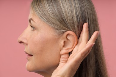 Photo of Sound. Senior woman showing hand to ear gesture on pink background