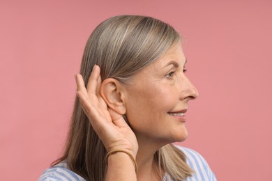 Photo of Sound. Senior woman showing hand to ear gesture on pink background