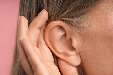 Photo of Sound. Senior woman showing hand to ear gesture on pink background, closeup