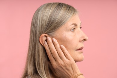 Photo of Sound. Senior woman touching her ear on pink background
