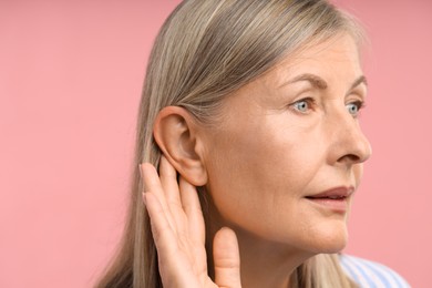 Photo of Sound. Senior woman touching her ear on pink background