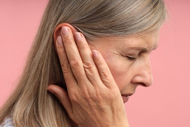 Photo of Sound. Senior woman touching her ear on pink background