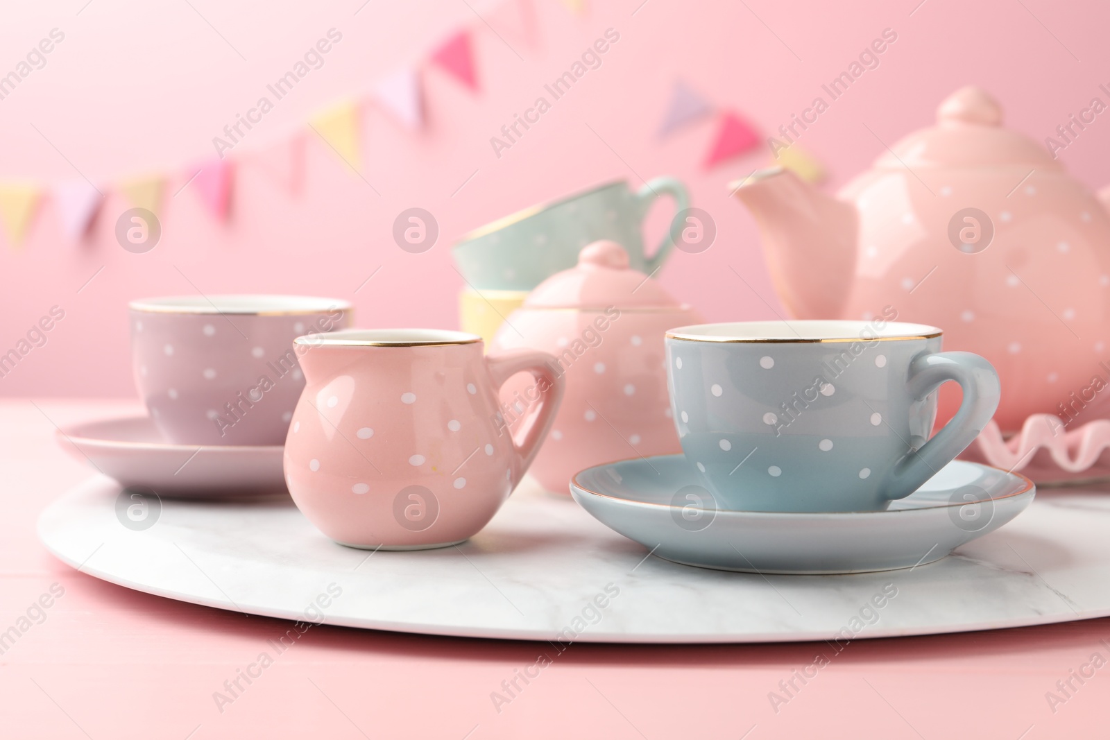 Photo of Beautiful ceramic tea set for children on wooden table against pink background with party flags, closeup