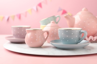 Photo of Beautiful ceramic tea set for children on wooden table against pink background with party flags, closeup