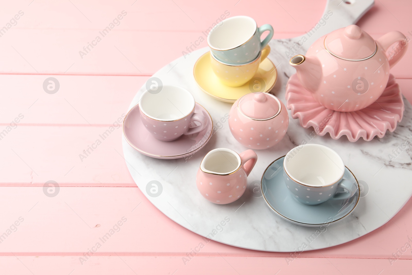 Photo of Beautiful ceramic tea set for children on pink wooden table. Space for text