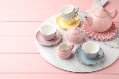 Photo of Beautiful ceramic tea set for children on pink wooden table. Space for text