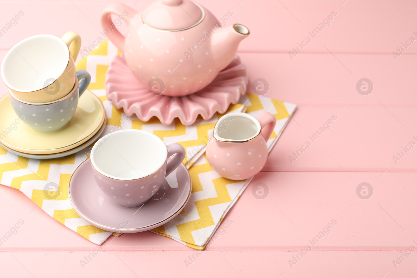 Photo of Beautiful ceramic tea set for children on pink wooden table. Space for text