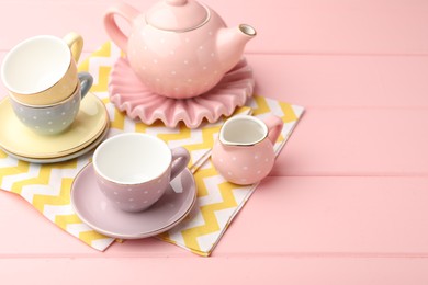 Photo of Beautiful ceramic tea set for children on pink wooden table. Space for text