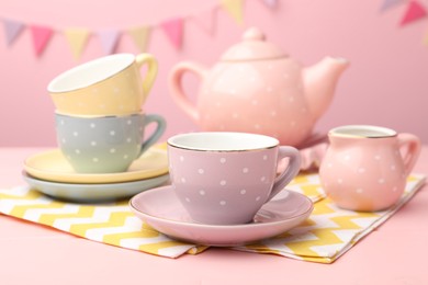Photo of Beautiful ceramic tea set for children on wooden table against pink background with party flags, closeup