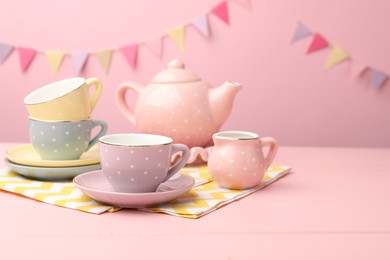 Photo of Beautiful ceramic tea set for children on wooden table against pink background with party flags, closeup. Space for text