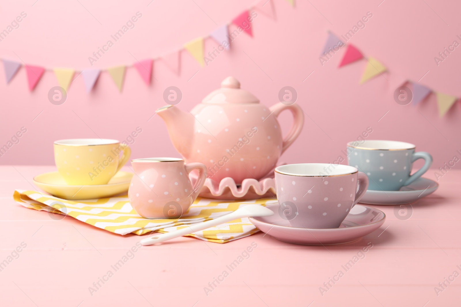 Photo of Beautiful ceramic tea set for children on wooden table against pink background with party flags, closeup