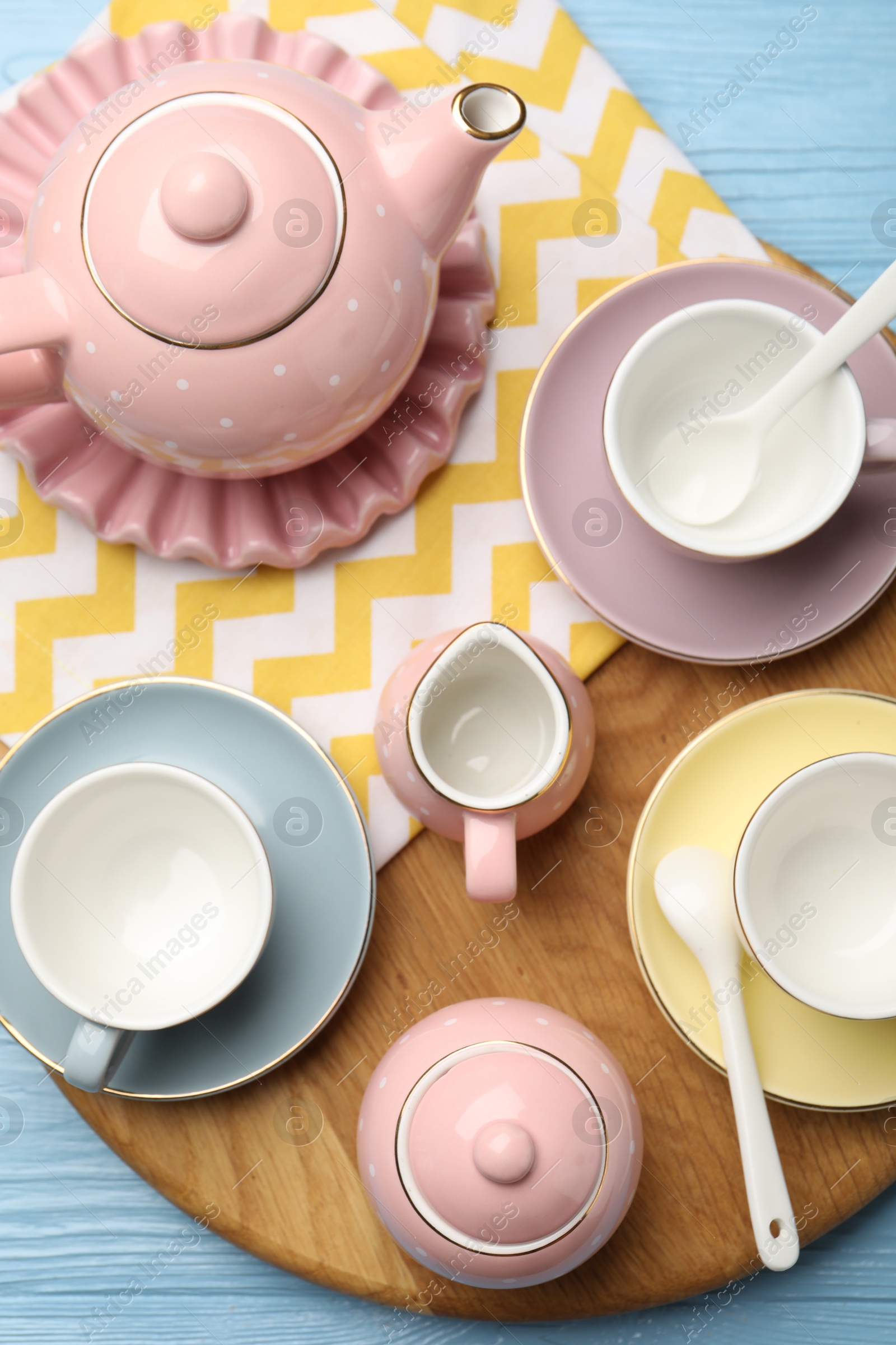 Photo of Beautiful ceramic tea set for children and napkin on light blue wooden table, top view