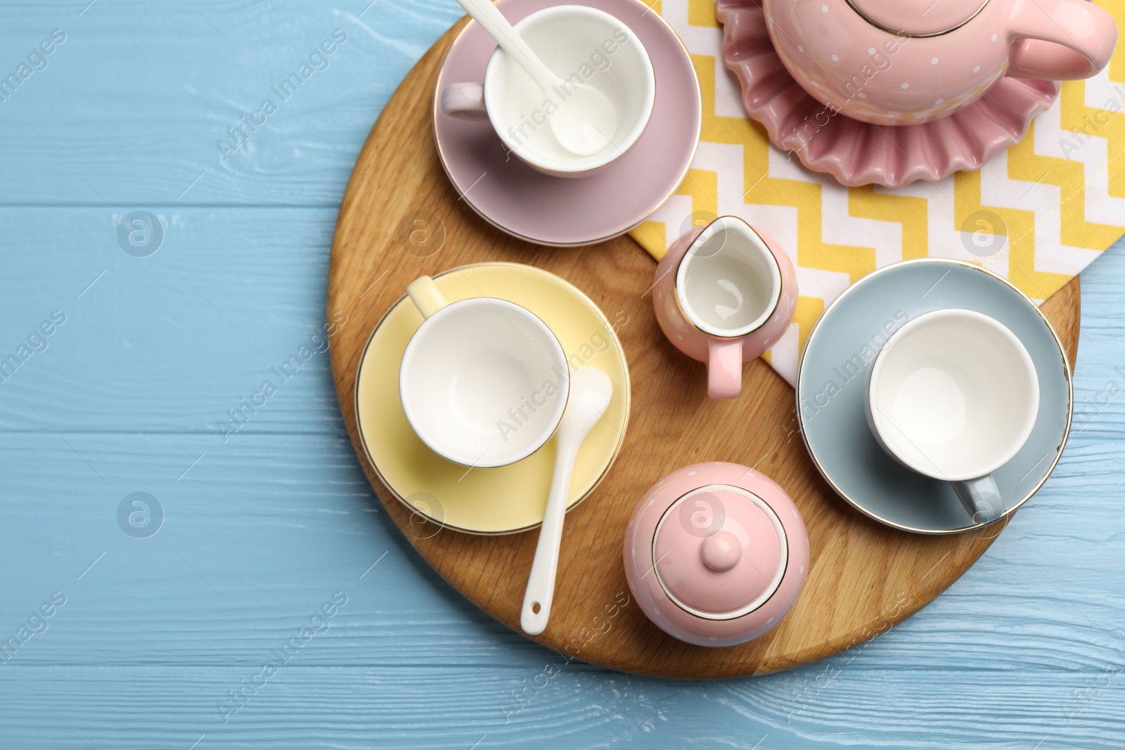Photo of Beautiful ceramic tea set for children and napkin on light blue wooden table, top view. Space for text
