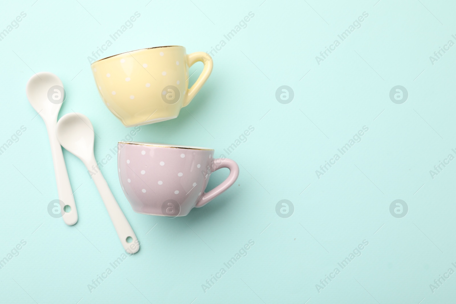 Photo of Ceramic tea set for children. Beautiful cups and spoons on turquoise background, flat lay with space for text