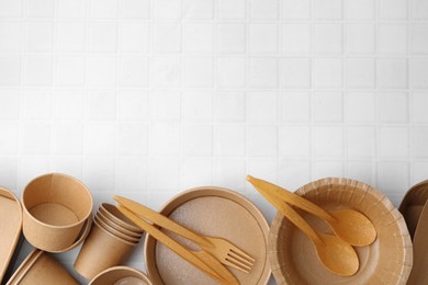 Photo of Set of disposable tableware on white tiled table, flat lay. Space for text