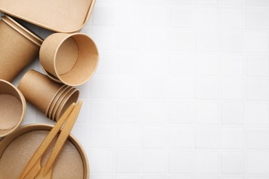 Photo of Set of disposable tableware on white tiled table, flat lay. Space for text