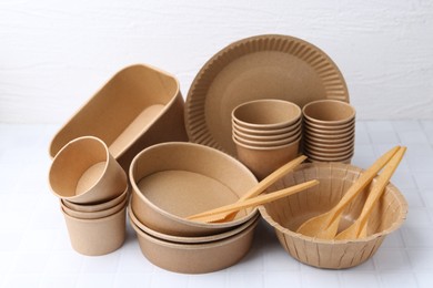 Photo of Set of disposable tableware on white tiled table, closeup