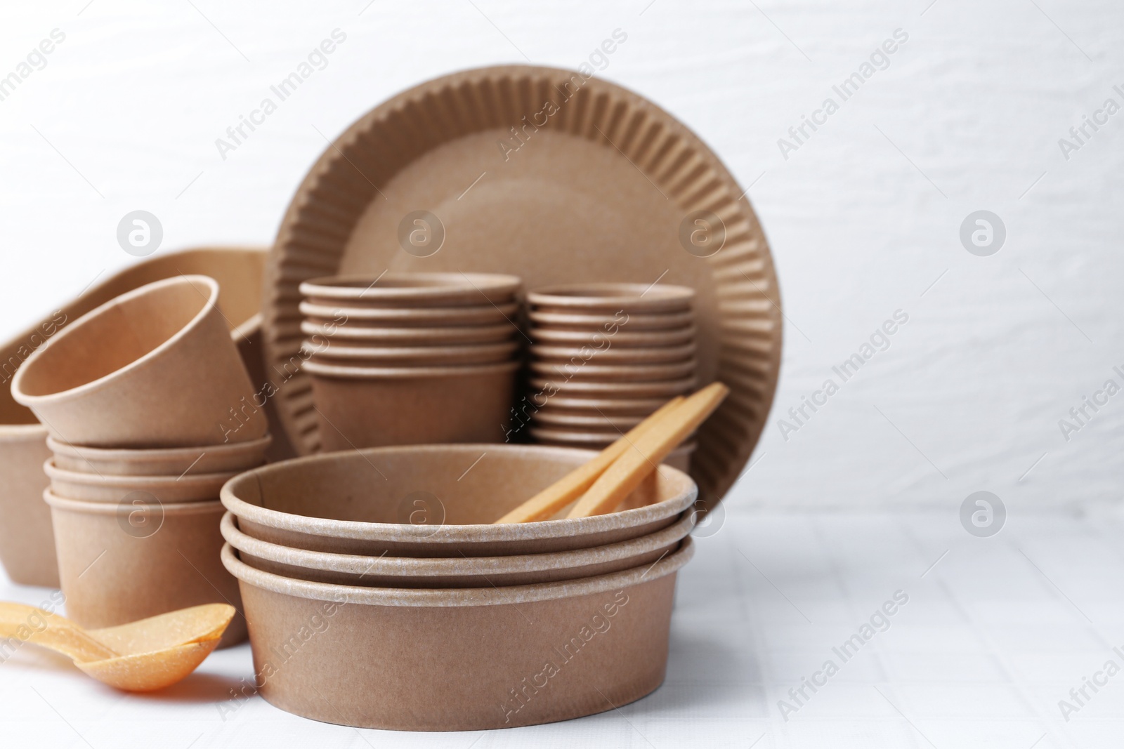 Photo of Set of disposable tableware on white tiled table, closeup. Space for text