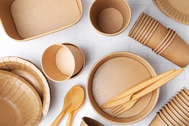 Photo of Set of disposable tableware on white tiled table, flat lay