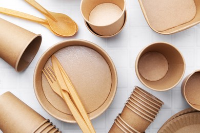 Photo of Set of disposable tableware on white tiled table, flat lay
