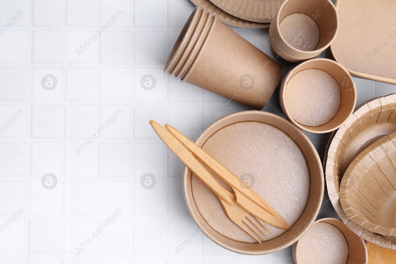 Photo of Set of disposable tableware on white tiled table, flat lay. Space for text
