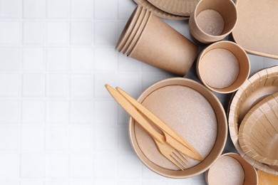 Photo of Set of disposable tableware on white tiled table, flat lay. Space for text