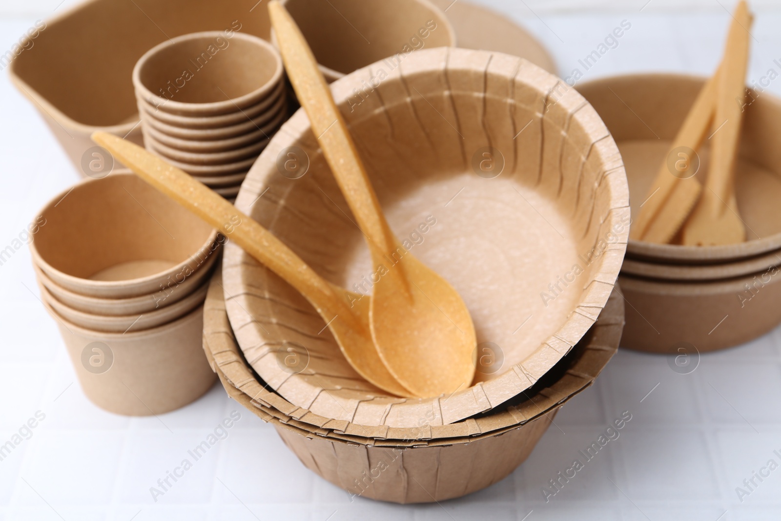 Photo of Set of disposable tableware on white tiled table, closeup