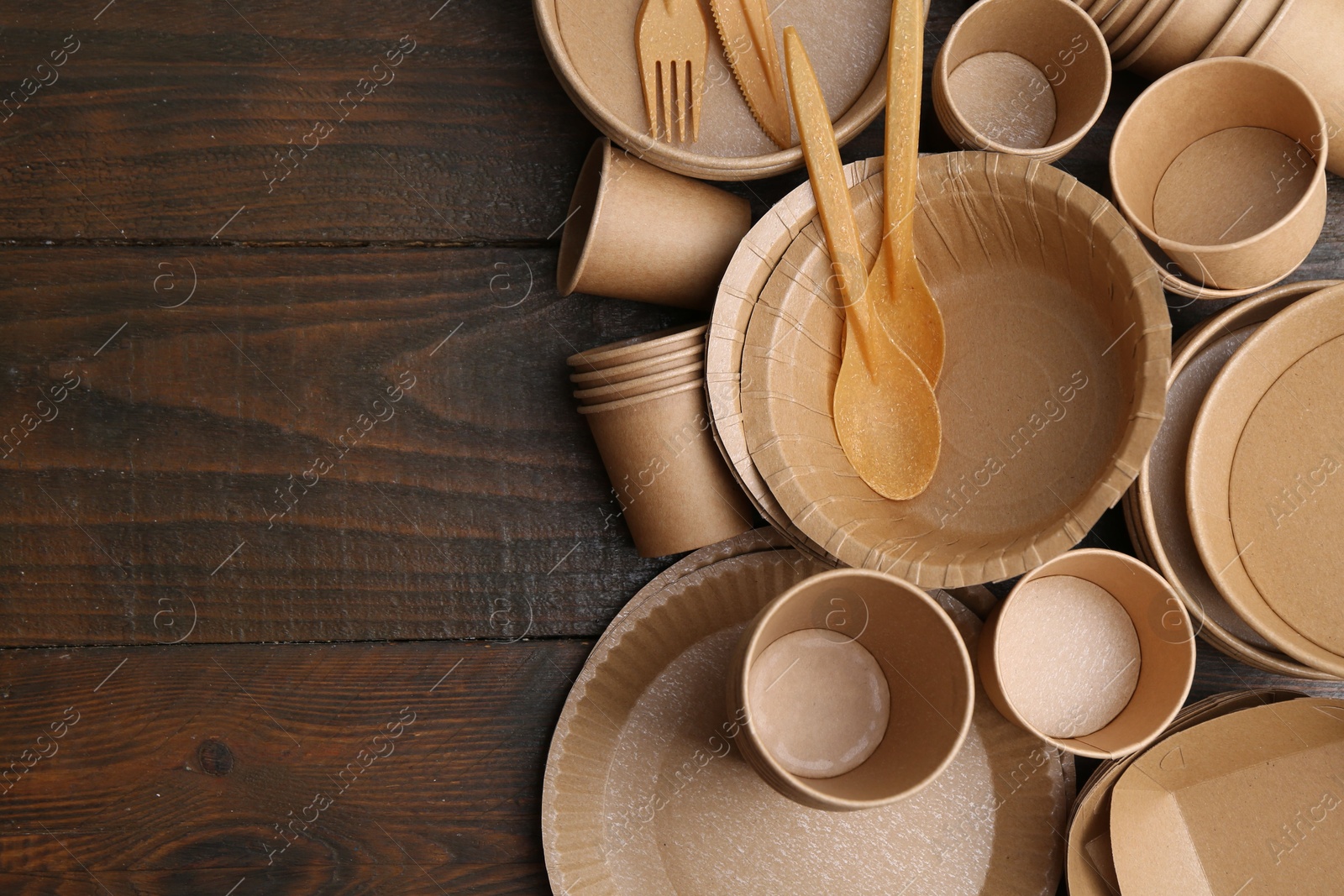 Photo of Set of disposable tableware on wooden table, flat lay. Space for text