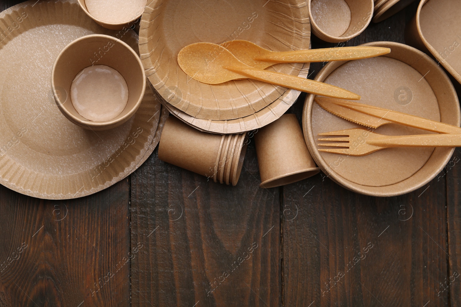 Photo of Set of disposable tableware on wooden table, flat lay. Space for text