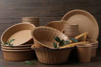 Photo of Set of disposable tableware and green leaves on wooden table, closeup