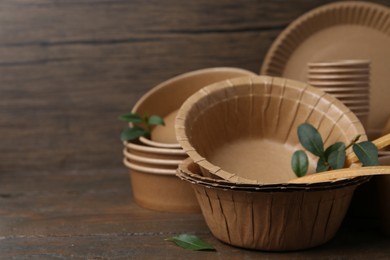 Photo of Set of disposable tableware and green leaves on wooden table, closeup. Space for text