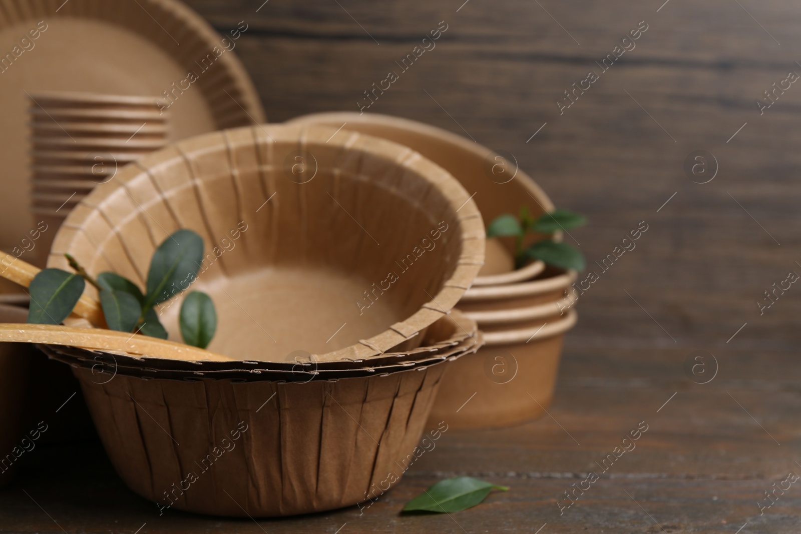 Photo of Set of disposable tableware and green leaves on wooden table, closeup. Space for text